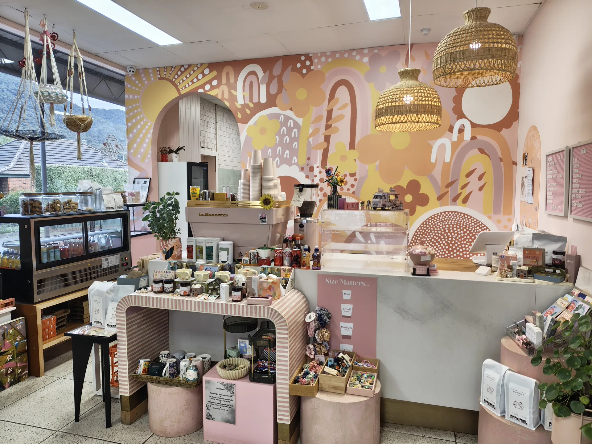 Inside Posie Project in daylight — pastel botanical mural, rattan pendant lights and the cafe counter