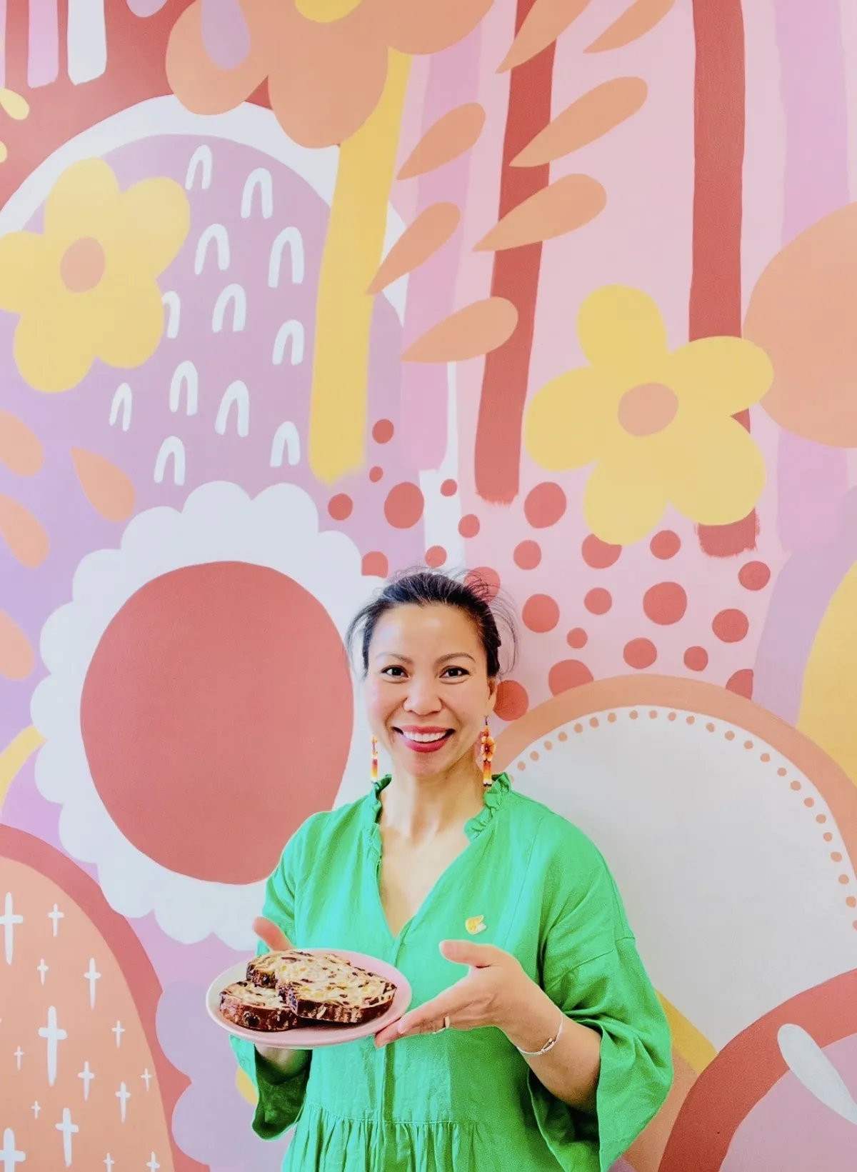 Lan smiling with a coffee cup in front of the cafe’s floral mural